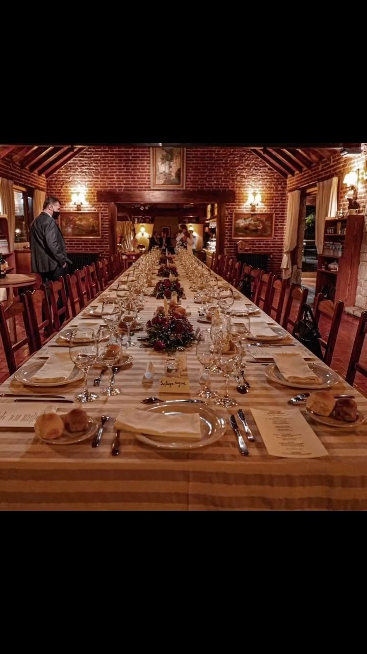 Mesa larga preparada con vajilla, copas y flores en el salón de eventos